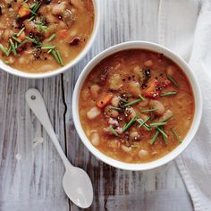 two bowls filled with soup sitting on top of a wooden table next to a spoon