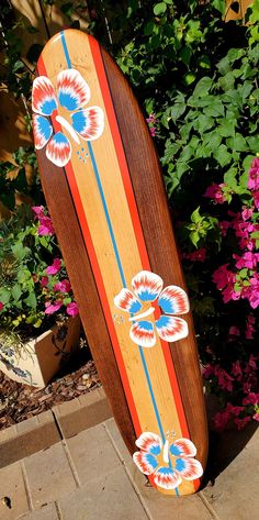 a skateboard with flowers painted on it sitting in front of some bushes and pink flowers