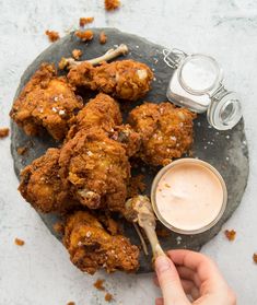 a person holding a spoon over some fried food on a stone platter with dipping sauce