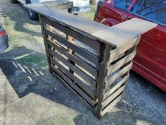 a red car is parked next to a wooden crate that has been placed on the ground