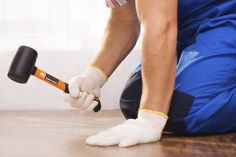 a man in blue overalls and white gloves is using a hammer on the floor