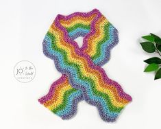 a crocheted rainbow scarf next to a plant