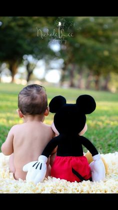 a baby sitting next to a mickey mouse stuffed animal