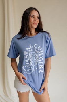 Introducing our Coastal Cowgirl Light Blue Graphic Tee, where western charm meets coastal cool for an effortlessly chic look. Crafted from soft and breathable light blue fabric, this tee offers both style and comfort for any occasion. At the heart of its design is a striking white cowgirl boot graphic, capturing the essence of western spirit and adventure. Wrapped around the boot, the "Coastal Cowgirl" text in crisp white adds a touch of seaside flair, blending rugged charm with laid-back coasta Washed Blue Relaxed Fit Graphic Tee, Soft-washed Light Wash Short Sleeve Tops, Washed Blue Relaxed Fit Graphic Top, Relaxed Fit Washed Blue Graphic Print Top, Light Blue Graphic Tee With Relaxed Fit, Washed Blue Graphic Tee With Print, Washed Blue Graphic Tee With Graphic Print, Light Wash Short Sleeve Graphic Tee, Light Wash Graphic Tee With Short Sleeves