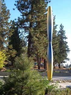 a tall metal sculpture sitting in the middle of a forest next to a road and trees