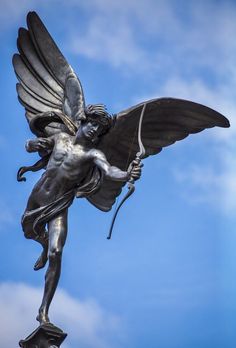 a statue of an angel holding a bow and arrow on top of a building with blue sky in the background