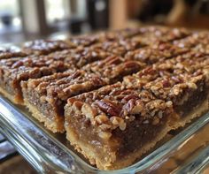 a glass dish filled with pecan bars on top of a wooden table