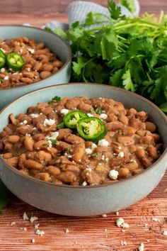 two bowls filled with beans and vegetables on top of a wooden table next to parsley