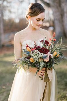 a woman holding a bouquet of flowers in her hands and wearing a dress with sheer sleeves