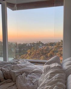 an unmade bed sitting in front of a window with the sun setting on it