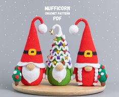 three crocheted christmas gnomes sitting next to each other on a wooden platter