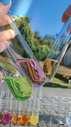 two people holding glasses filled with different colored liquids in front of each other on a metal rack