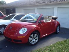 a red convertible car parked in front of a house with two other cars behind it