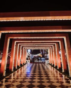 an entrance to a building lit up at night with lights on the pillars and checkered floor