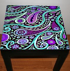 an artistically designed table with purple and blue designs on it, sitting on a wooden floor