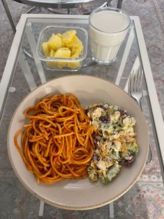 a bowl of spaghetti, salad and milk on a glass table