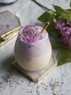 a purple drink sitting on top of a white table next to flowers and a gold tray