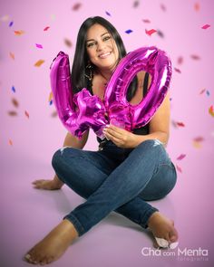 a woman sitting on the floor holding two large pink balloons