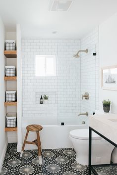 a white bathroom with black and white tile flooring, shelving units and a wooden stool