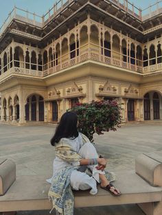 a woman is sitting on a bench in front of a large building with balconies