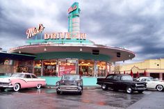 several old cars parked in front of a drive - in restaurant on a cloudy day