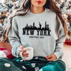 a woman sitting in front of a christmas tree wearing a sweatshirt that says new york