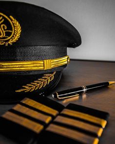 a black and yellow hat with gold trim next to a pen on a wooden table