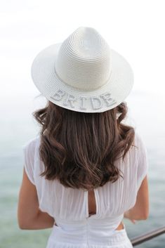 Keep the sunshine out of your eyes this summer with Shiraleah's "Bride" Rhinestone Hat. Made from ivory paper straw with the word "Bride" embroidered in faux pearls and rhinestones, this elegant beach hat is the perfect match to any honeymoon outfit. Pair with other items from Shiraleah's Hitched Collection to complete your look! Features A Crisp Ivory Color With A Rhinestone Stripe Detail And The Word "Bride" Embroidered In Faux Pearls Shiraleah Is A Trend-Driven Lifestyle Brand Focused On The Little Gifts That Make Life Special! Made From Paper Straw, Rhinestones, And Faux Pearls One Size And Adjustable Made In China Summer Hats With Rhinestones And Short Brim, Rhinestone Hat, Sequin Hat, Honeymoon Outfits, Accessories Display, Faux Fur Pom Pom, Beach Hat, Cold Weather Accessories, Summer Hats