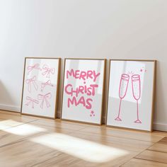 three framed christmas cards on the floor in front of a white wall with pink lettering