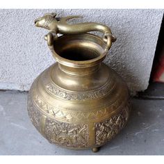 an ornate brass vase with a snake on the top is sitting next to a wall