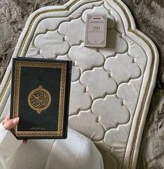 a person holding up a book in front of a white bed with gold trimmings