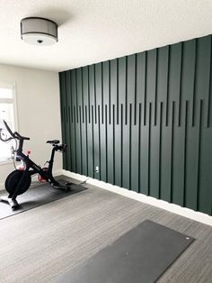 an exercise room with a stationary bike in front of a green paneled wall and yoga mat on the floor