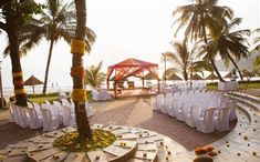 an outdoor ceremony setup with white chairs and flowers on the ground, surrounded by palm trees