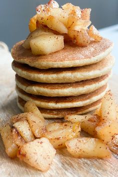 a stack of pancakes topped with sliced apples and cinnamon on a wooden table next to some pieces of fruit