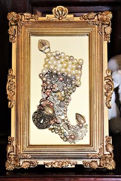 an ornate gold frame with pearls and other items in it on a shelf next to a stuffed animal