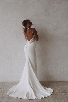 a woman in a white wedding dress is standing against a wall with her back to the camera