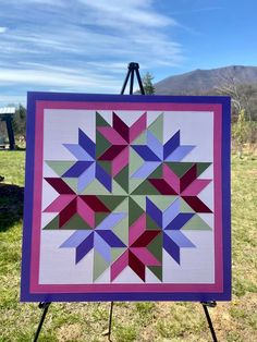 a colorful quilt hanging on a easel in the grass