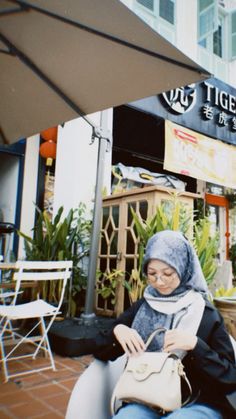 a woman sitting on a bench in front of a building with an umbrella over her head