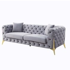 a grey couch with gold legs and buttons on the back, sitting in front of a white background