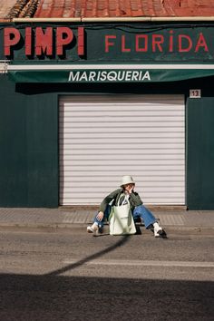 a man sitting on the sidewalk in front of a building with a sign that reads pimpi florida