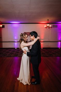 a bride and groom share their first dance at the wedding reception in front of purple lights