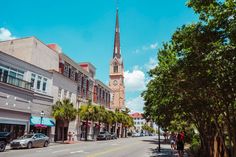 people are walking down the street in front of some buildings and a church steeple