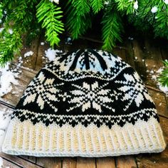 a black and white knitted hat sitting on top of a wooden floor next to snow