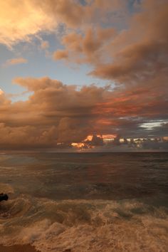 the sun is setting over the ocean with clouds in the sky and waves crashing on the shore