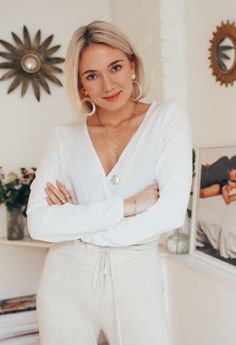 a woman standing in front of a wall with her arms crossed and looking at the camera