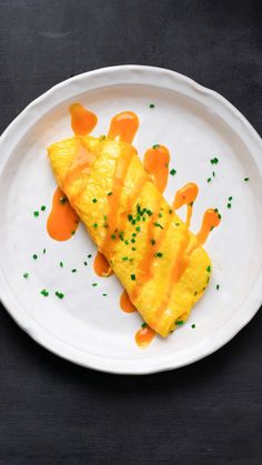 an omelet on a white plate with orange sauce and green sprinkles