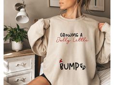 Surprise everyone this holiday season with our funny and cozy Christmas pregnancy sweatshirt reveal gift! This soft pregnancy reveal sweater is perfect for sharing the big news in a fun way. With a clever design, it's a playful pregnant announcement crewneck that will get smiles all around. Ideal for chilly days, this funny maternity fall shirt lets you show off your bump in style. Whether you're expecting or shopping for a mom-to-be, this preggers sweatshirt is the perfect festive addition to your wardrobe!   *Fast shipping in 2-5 Business Days! *Comfy unisex sweatshirts are soft and durable. *Measuring tip: Take your favorite sweatshirt or tee, lay it on a flat surface and measure the width (armpit to armpit) and length (top to bottom), then compare with our size chart. *Classic fit, dur Pregnant Christmas Outfit Funny, Pregnant Holiday Shirt, Pregnant Christmas Shirts, Pregnant Christmas Shirt, Pregnancy Ugly Christmas Sweater, Pregnancy Sweatshirt, Pregnant Announcement, Christmas Maternity Shirt, Funny Maternity