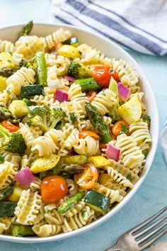 a bowl filled with pasta and vegetables on top of a blue tablecloth next to a fork