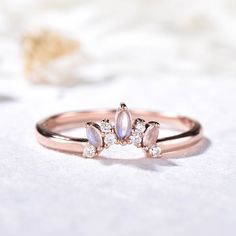 a rose gold ring with three pear shaped diamonds on the front and side, sitting on a white surface