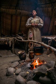 a woman standing next to a fire in a hut